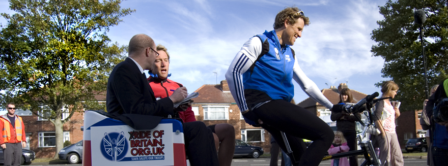 Olympic gold medalist James Cracknell pedals, while TV presenter Ben Fogle speaks to a reporter seated on the back of a Bugbugs rickshaw